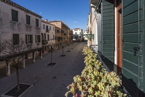 A narrow street with buildings on both sides, featuring a row of trees and a green door on the right.