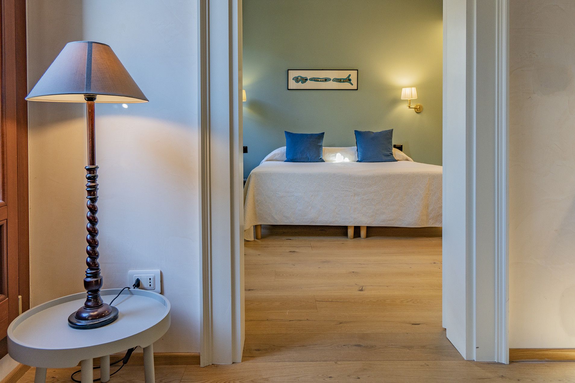 A hotel room with a bed, a bedside table with a lamp, and a wall-mounted light fixture.