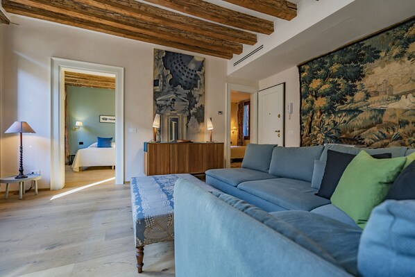 A modern living room with a large blue sofa, a wooden ceiling, and a large tapestry on the wall.