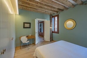 A bedroom with a bed, a desk, and a chair. There is a door leading to another room.