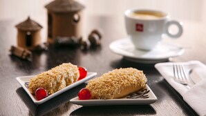 Dois doces em pratos, com uma xícara de café e um pequeno bebedouro de pássaros ao fundo.