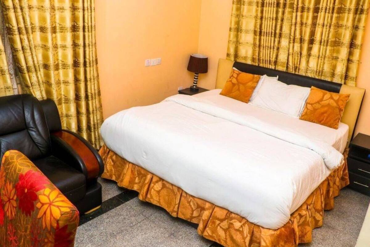 Ein Hotelzimmer mit Bett, Sessel, Nachttisch und Vorhängen.
