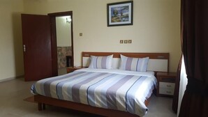 Quarto com cama, mesa de cabeceira, cabeceira de madeira, um quadro na parede e uma porta.