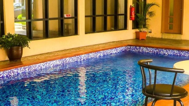 Piscina interior com borda azulejada, um extintor de incêndio e um vaso de planta.