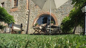 Ein Sitzbereich im Freien mit einem Steinhaus, einem großen Sonnenschirm und einer Rasenfläche.