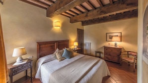 Ein Schlafzimmer mit Holzboden, einem Bett mit Kissen, einem Nachttisch mit Lampe, einem Schminktisch und einem Sessel.