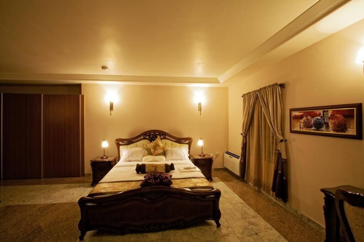 A bedroom with a large bed, two bedside tables, a wardrobe, and a painting on the wall.