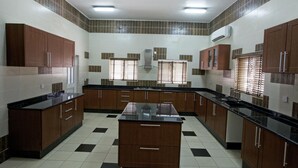 A kitchen with a central island, dark wooden cabinets, and a black countertop. - Oxygen Holiday Resort (Owerri)