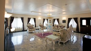 A spacious living room with a high ceiling, elegant furniture, and large windows with curtains. - Oxygen Holiday Resort (Owerri)