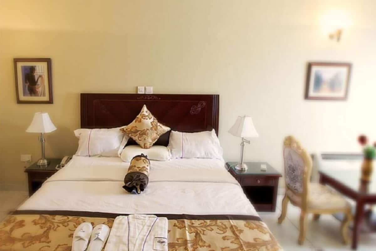 A hotel room with a bed, two bedside tables, a chair, and a desk with a lamp.