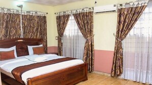 A bedroom with a wooden bed, patterned curtains, and an air conditioning unit. - Everyday Check Inn Limited (Port Harcourt)