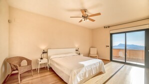 A bedroom with a bed, a chair, a bedside table, a ceiling fan, and a large sliding glass door leading to a balcony with a view. - Beautiful villa with private pool and sea views in Altea, Ref 3030 Elena Hills (Altea)