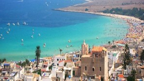 A coastal town with a beach, boats, and a prominent building with a tower.