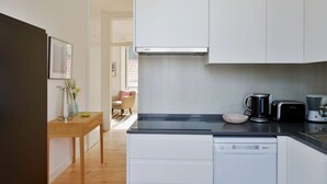 Eine kompakte Küche mit weißen Schränken, einer schwarzen Arbeitsplatte, einer Kaffeemaschine, einem Toaster und einem Geschirrspüler.