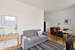 A modern living room with a grey sofa, wooden desk, and dining area.