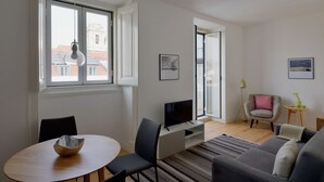 Ein modernes Wohnzimmer mit Essbereich, Fernseher und großem Fenster mit Blick auf Gebäude.