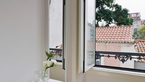 Ein Balkon mit weißer Brüstung, freier Blick auf das roter-Ziegeldach eines Gebäudes gegenüber und eine weiße Wand.
