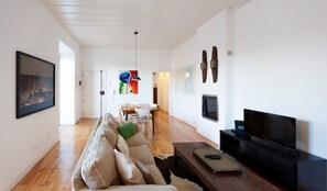 A spacious living room with a sofa, a coffee table, a TV, and a dining area with a table and chairs. - FLH São Jorge Castle Flat (Lisbon)