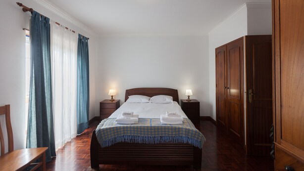 Un dormitorio ordenado con cama, lámparas de noche, un armario de madera y una colcha a cuadros.