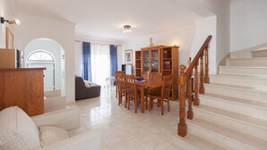Amplia sala de estar con mesa de comedor, sillas, sofá, aparador de madera y una escalera.