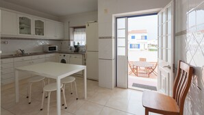 Una cocina con armarios blancos, un microondas, un refrigerador y un comedor con una mesa y sillas.