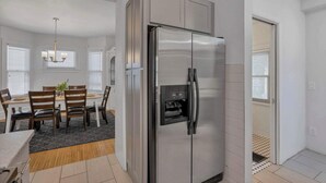 Une cuisine moderne avec un réfrigérateur en acier inoxydable, une table à manger en bois et des chaises, ainsi qu’un lustre.