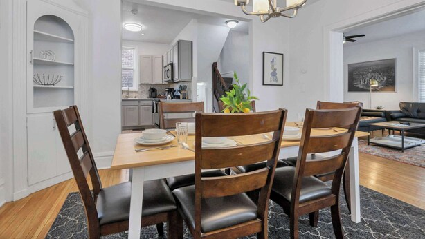 Un coin repas avec une table et des chaises en bois, un lustre et une cuisine en arrière-plan.