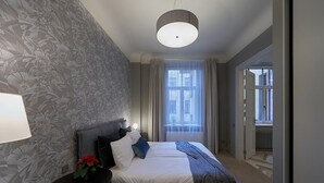 Un dormitorio con cama, mesita de noche, lámpara y ventana con cortinas.