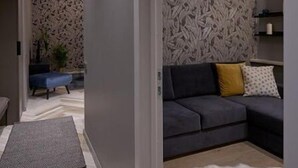 Una sala de estar moderna con un sofá gris, un tapete blanco y mullido, y un papel tapiz estampado.