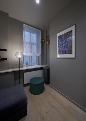 Une chambre moderne avec une fenêtre, un tableau abstrait encadré, une lampe sur pied et un pouf vert.