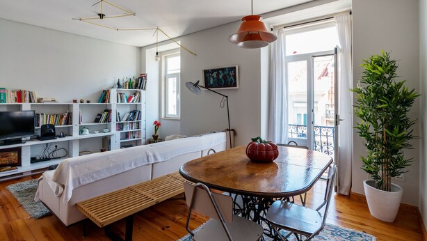 A living room with a wooden table, a sofa, a bookshelf, a TV, and a potted plant.
