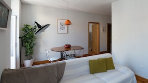 A modern living room with a sofa, a dining table, a potted plant, and a pendant light.