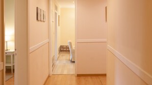 A hallway with a wooden floor, white walls, and a door leading to a bathroom.