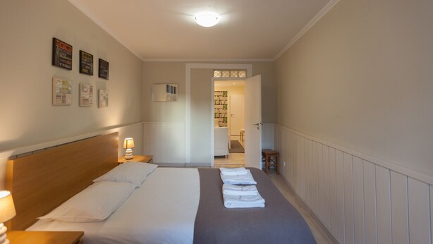 A hotel room with a large bed, a bedside table with a lamp, a wooden headboard, and a view into the bathroom through an open door.