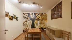 A dining area with a wooden table and chairs, a wall mural of a tree, and a light fixture above.