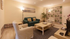 A living room with a green sofa, white armchairs, a coffee table, and a bookshelf.