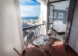 Een balkon met een eettafel, een bed met wit beddengoed en uitzicht op zee.
