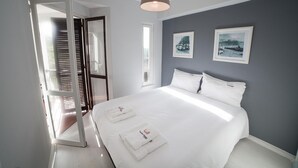 Ein modernes Schlafzimmer mit einem großen Bett, weißen Bettwäsche, zwei gerahmten Bildern an der Wand und einer Deckenleuchte.