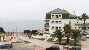 Un edificio frente al mar con techo verde, zona de estacionamiento y palmeras.