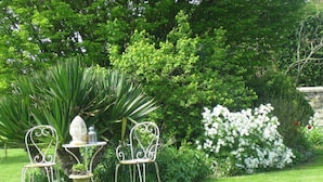 A garden with a table and two chairs, surrounded by lush greenery and white flowers. - Le Clos Xavianne (Ribécourt-la-Tour)