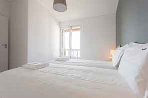 A hotel room with two beds, a window with blinds, and a lamp on the nightstand.