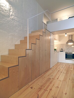 A modern kitchen with wooden flooring, a built-in oven, and a staircase with wooden steps. - FLH Porto Modern Flat (Oporto)