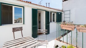 A small, white building with green shutters, a wooden bench, and a small table.