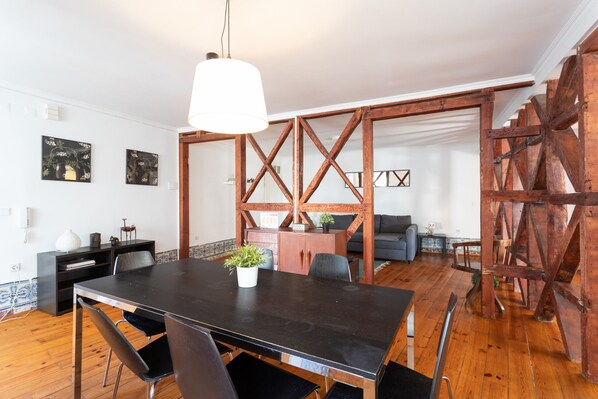 A dining area with a large table, chairs, and a hanging light fixture.