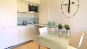 Una cocina moderna con armarios blancos, un microondas de acero inoxidable, una mesa de vidrio y dos plantas en macetas.
