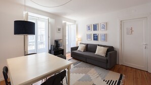Una sala de estar moderna con un sofá, una mesa de comedor y un televisor. Hay cuadros enmarcados en la pared y una puerta con cerradura.