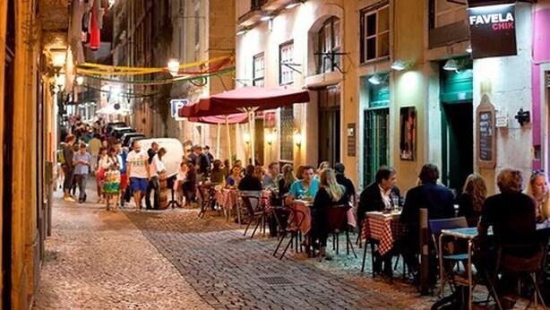 Una calle concurrida con mesas al aire libre en un restaurante, una multitud de gente y un edificio con un letrero que dice "FAVELA CHIK".