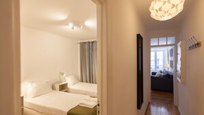 Habitación de hotel con dos camas, un pasillo que conduce a una sala de estar y una lámpara de araña moderna.