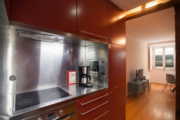 A compact kitchen with a stainless steel range, a coffee maker, and a microwave. There is a small seating area with a table and a chair.