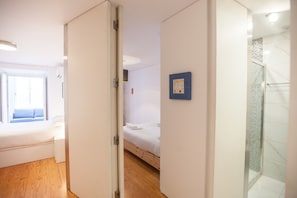 A hotel room with a bed, a small bedside table, a window with a view, and a bathroom with a shower.